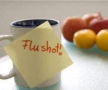 coffee mug that has a sticky note saying Flu shot! on it with fruit blurred in the background