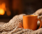 tan knit blanket with orange mug and fire in a fireplace in the background
