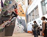 Barnes Center at The Arch climbing wall with person climbing wall and bystanders watching