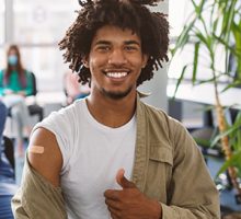 Person smiling after vaccine, revealing bandage on upper arm