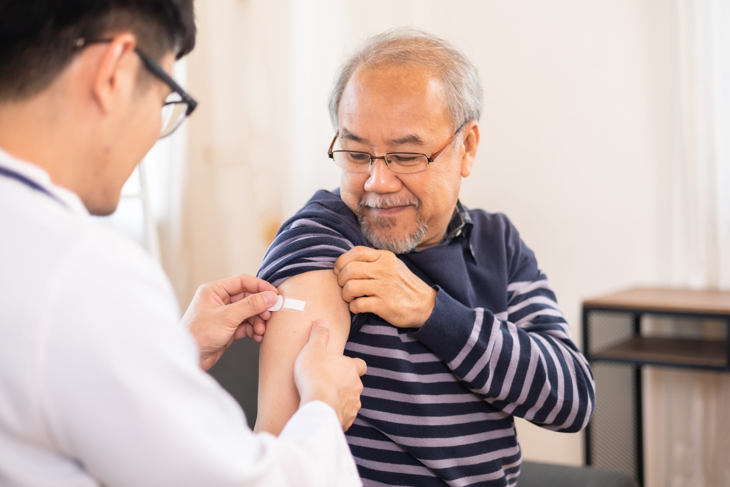 Person sitting and getting bandage on upper arm after flu vaccine clinic.